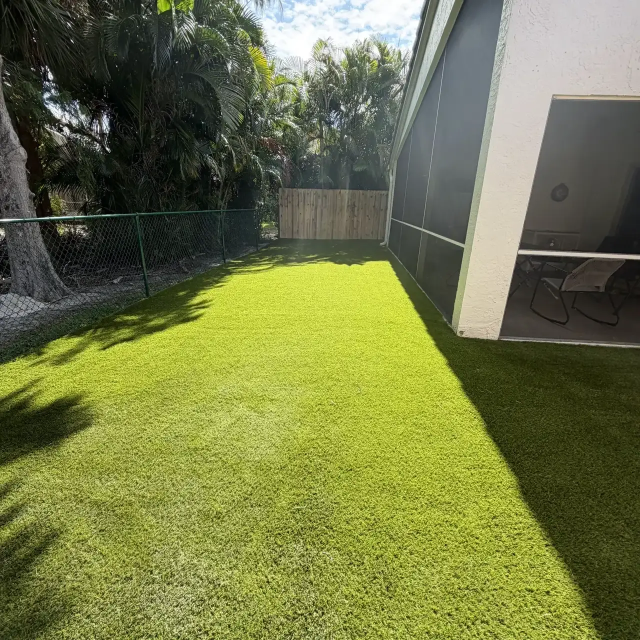 Artificial turf by screened patio with tropical landscaping